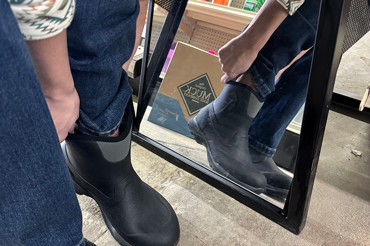 Someone trying on Muck brand boots in front of a mirror.